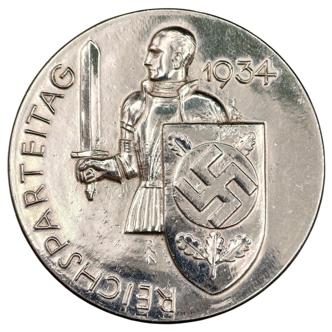 NSDAP Reichsparteitag 1934 Badge: A round tinnie-style badge commemorating the 1934 Reichsparteitag (Nuremberg Rally), featuring a medieval knight holding a sword and shield with a swastika emblem, surrounded by the inscription 'REICH