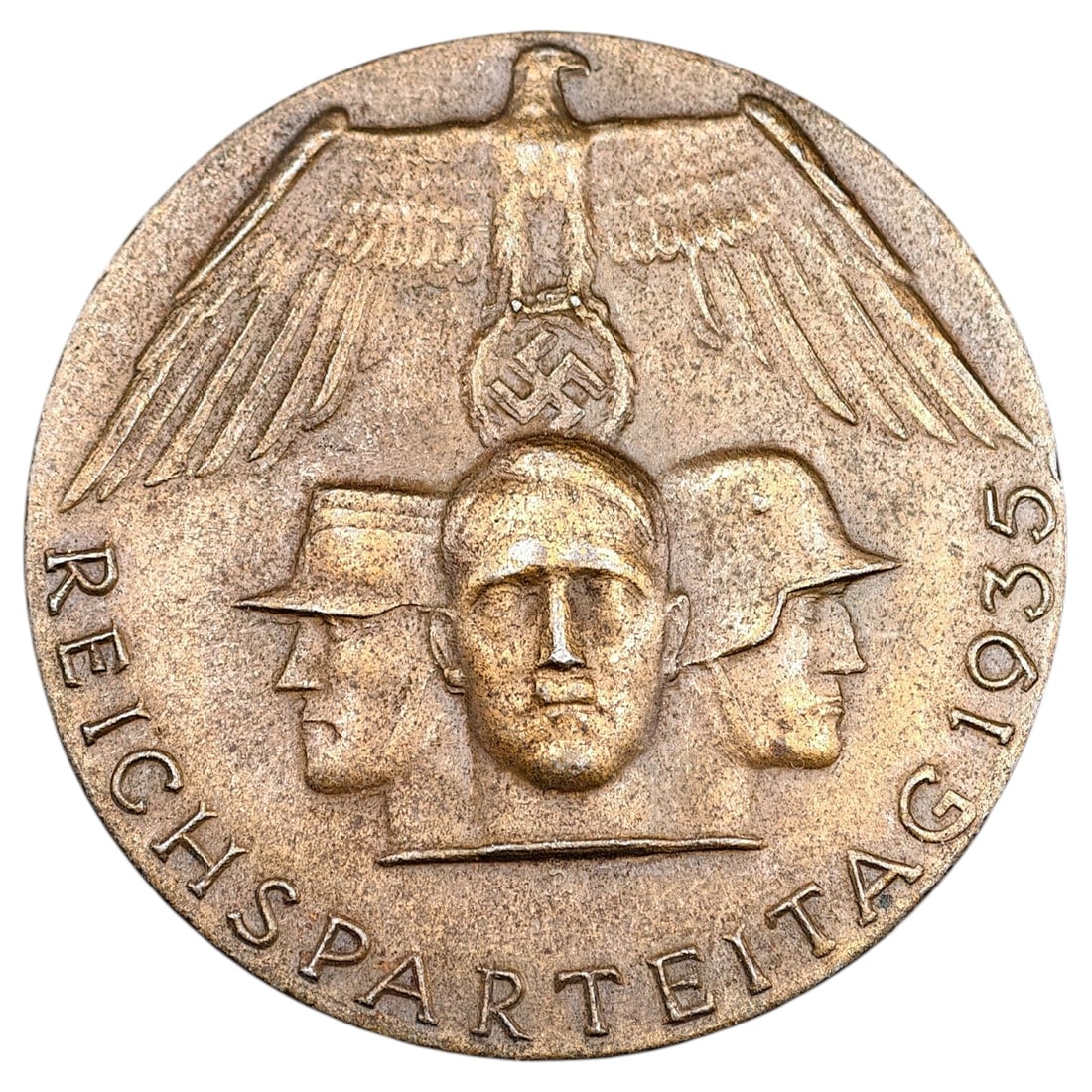 NSDAP Reichsparteitag 1935 Badge: A pin-back tinnie commemorating the 1935 Nazi Party Rally (Reichsparteitag) held in Nuremberg. The obverse depicts a stylized eagle with wings spread above three profile heads representing party, mili