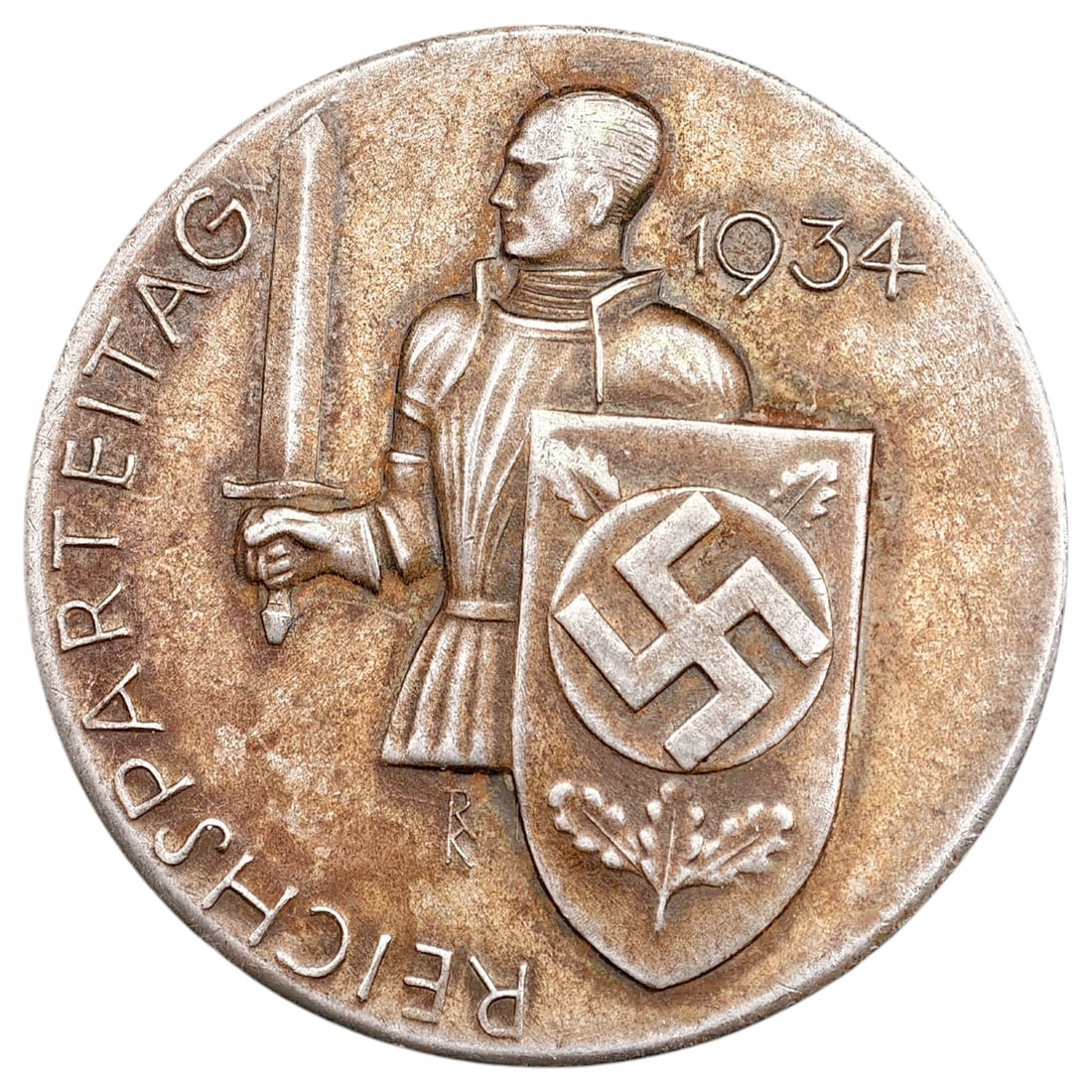 NSDAP Reichsparteitag 1934 Badge: A pin-back tinnie commemorating the 1934 Reichsparteitag (Nuremberg Rally), depicting a standard bearer holding a sword beside a shield with an oak leaf motif. The reverse bears the maker mark 'L. CHR