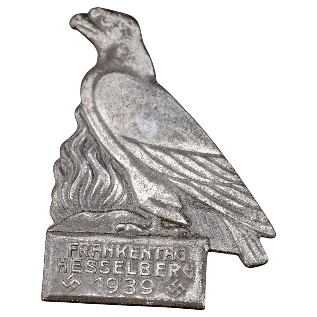 German Third Reich 'Frankentag Hesselberg 1939' Tinnie Badge by C. Balmberger, Nürnberg: A pressed metal tinnie badge featuring an eagle perched above a rectangular base inscribed 'FRANKENTAG HESSELBERG 1939' flanked by two swastikas. The reverse is maker-marked 'C. BALMBERGER NÜRNBERG'