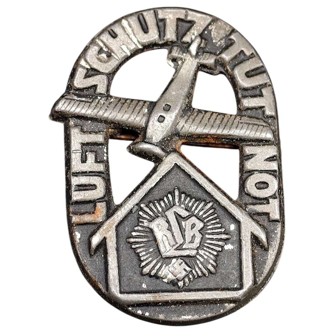 Third Reich Nazi Luftschutz RLB Tinnie Badge: A membership badge for the Reichsluftschutzbund (RLB) air raid protection organization, featuring an aircraft over a stylized house with the RLB emblem and swastika, with 'LUFTSCHUTZNOT' lettering aro