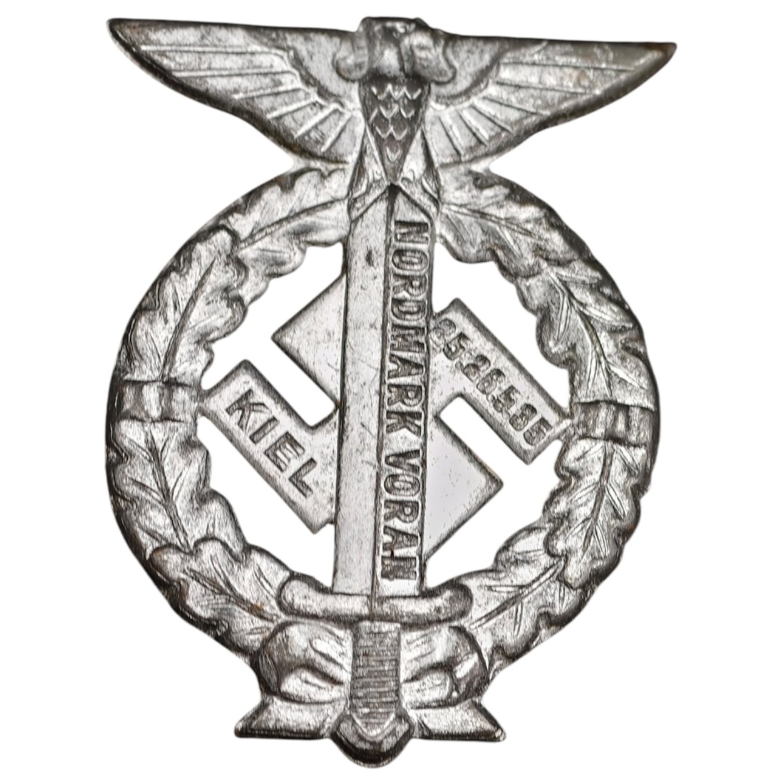 Third Reich Nazi Kiel Nordmark 1935 Tinnie Badge: A cast metal commemorative rally badge (tinnie) featuring a stylized eagle above an oak leaf wreath enclosing a swastika, sword, and diamond-shaped tablets inscribed 'KIEL', 'NORDMARK VORAN', and '25.