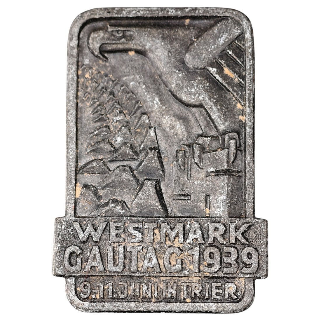 Third Reich Nazi 1939 Tinnie Badge: A pressed metal commemorative tinnie badge issued for the Westmark Gautag rally held 9-11 June 1939 in Trier. The obverse depicts a stylized eagle over a landscape with vineyards/hills and a searchlig