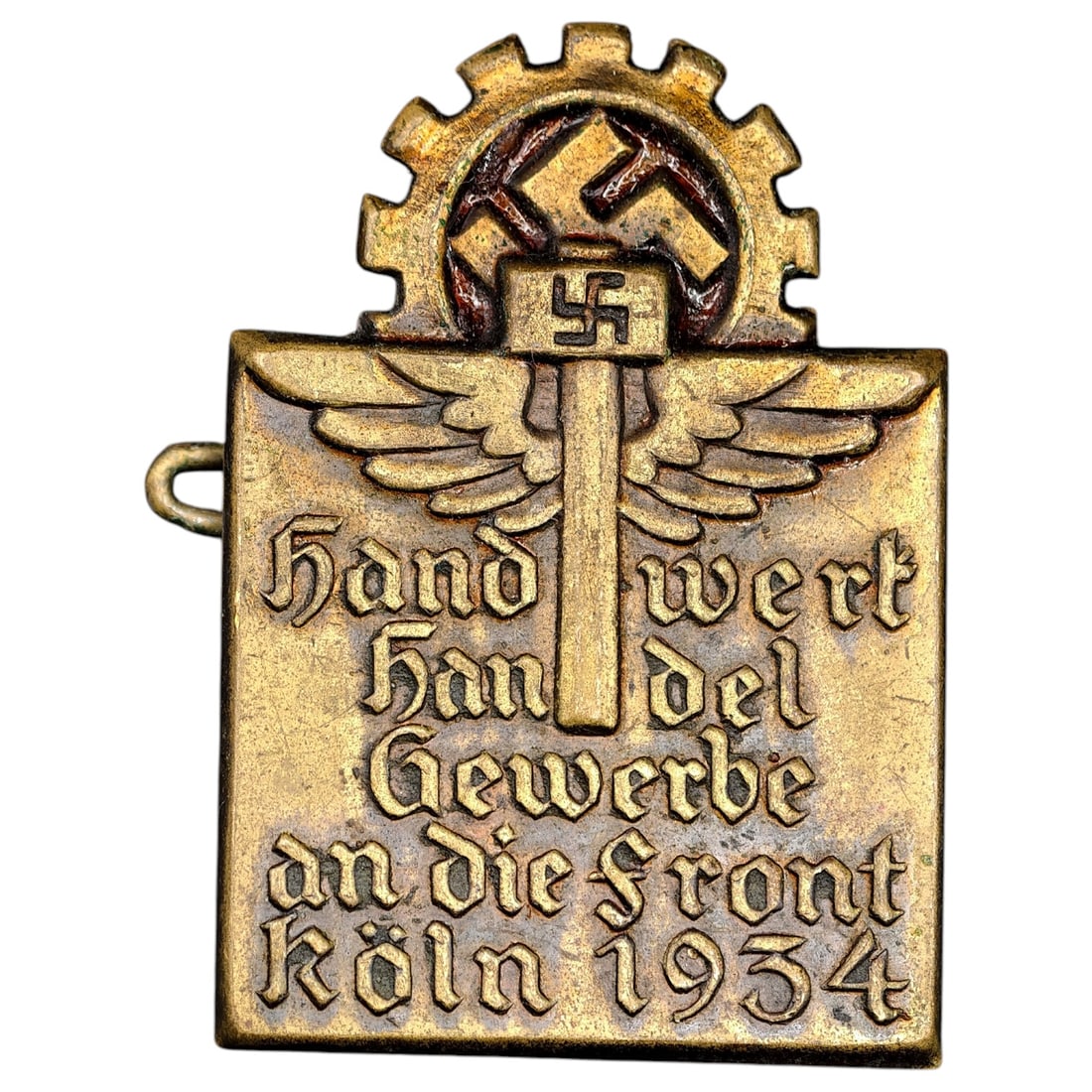Third Reich Nazi Koln 1934 Tinnie: A pin-back tinnie commemorating a 1934 Cologne (Köln) rally, reading 'Handwerk Handel Gewerbe an die Front Köln 1934', surmounted by a DAF (Deutsche Arbeitsfront) gear-and-wing emblem with central s