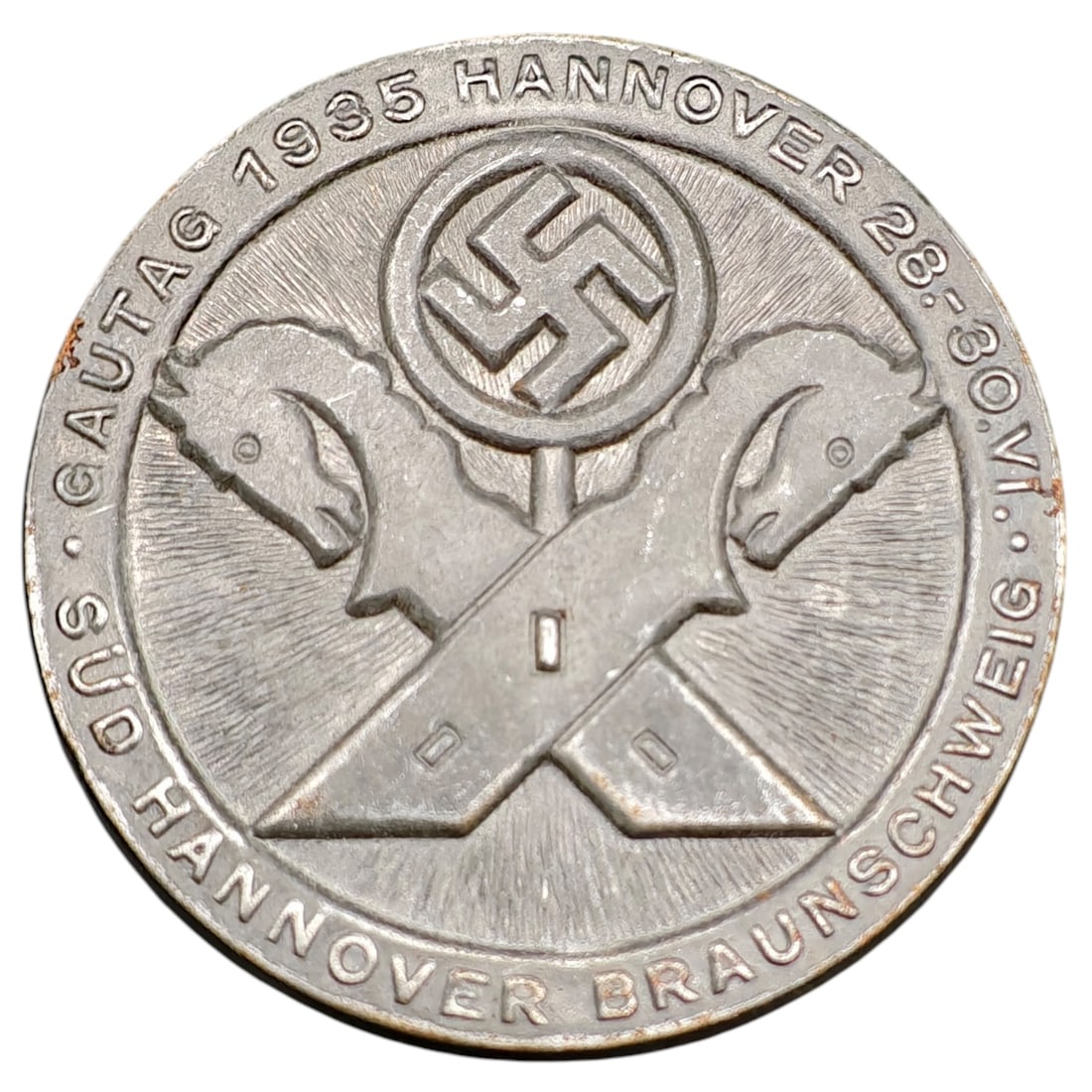 Third Reich Nazi Gautag 1935 Hannover Tinnie Badge: Round tinnie commemorating the Gautag rally held 28-30 June 1935 in Hannover, for Gau Süd-Hannover-Braunschweig. Obverse depicts a central swastika medallion above crossed horse-head symbols (referen