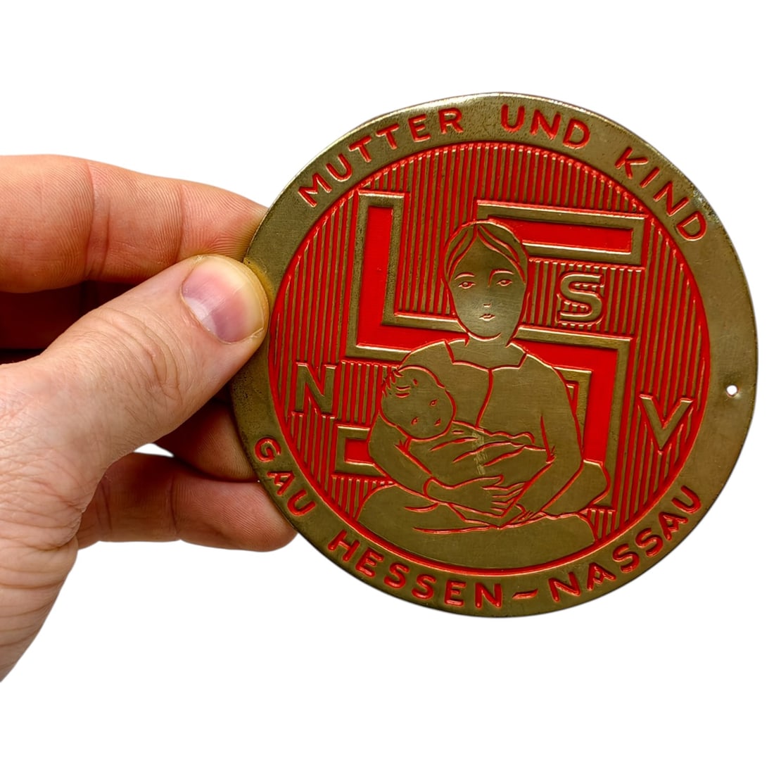 German WWII NSV National Socialist People’s Welfare Plaque: German WWII-era NSV (National Socialist People's Welfare) plaque or badge featuring a stylized mother holding a child, with a swastika and the letters NSV incorporated into the design. The outer