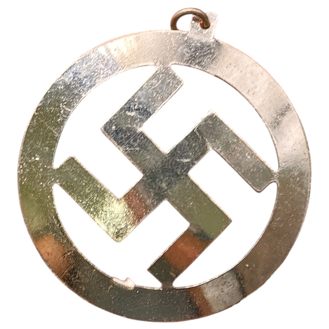 NSDAP Sympathizer Swastika Pendant: A round pierced metal pendant featuring an open-cut swastika motif within a circular border, fitted with a suspension loop for wear as a necklace charm. The piece appears to be a light-colored base me