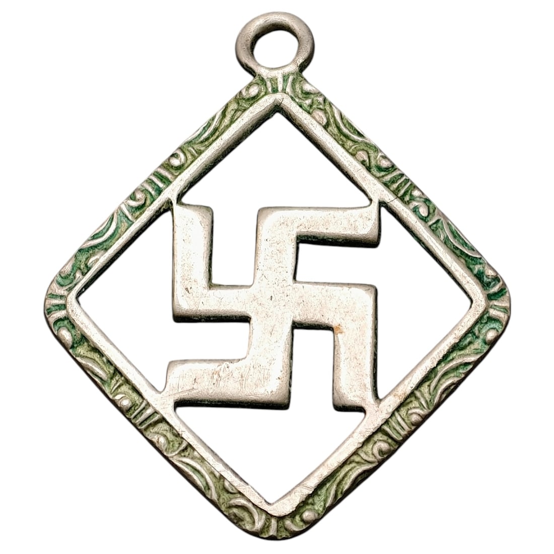 Third Reich Nazi Sympathizer Pendant: A pendant in what appears to be silver-tone metal, diamond-shaped, featuring an open-cut swastika motif at center, surrounded by a scrolling foliate border with green enamel accents. This style of