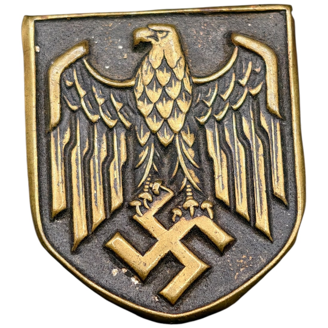 German WWII Wehrmacht Pith Eagle Shield: Shield-shaped tropical helmet insignia featuring the Wehrmacht eagle with wings spread, grasping a swastika, in metal that appears to be gilt-finished over a dark ground.