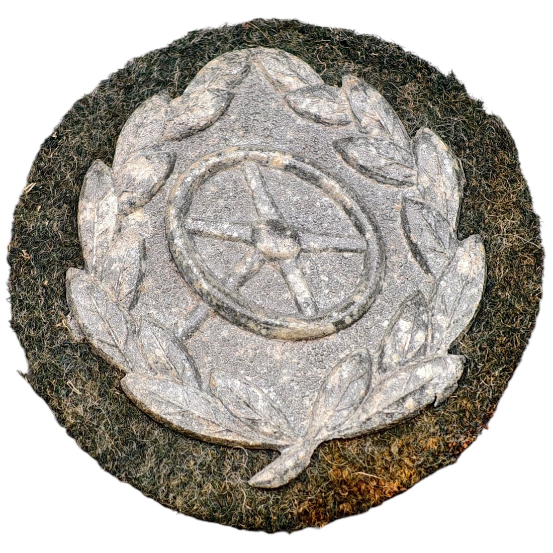 German WWII Drivers Proficiency Insignia: A pressed metal sleeve badge depicting a five-spoke steering wheel encircled by an oak leaf wreath, mounted on a round backing cloth. The badge shows a light gray/white painted or metalized finish typ