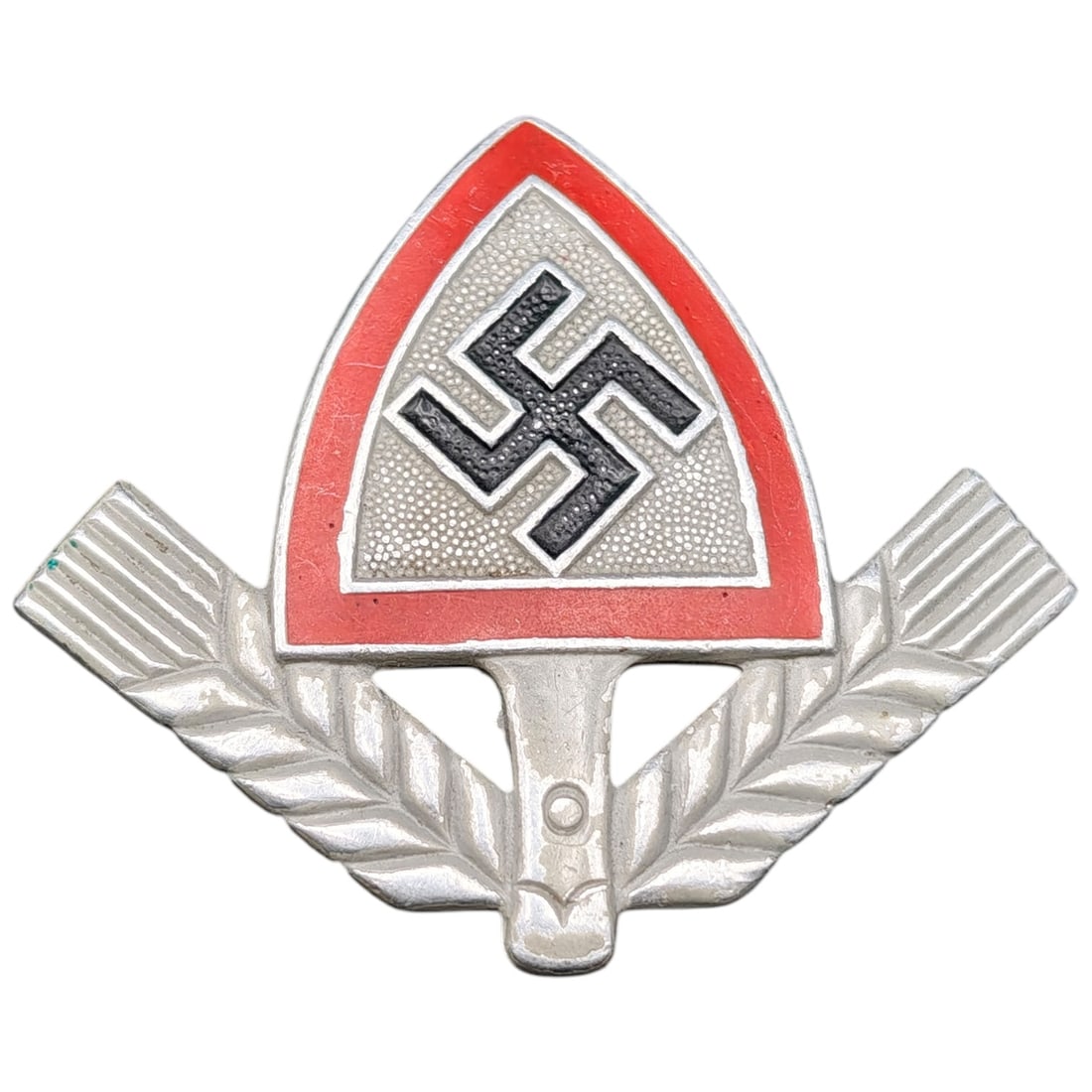 German WWII RAD Cap Visor Insignia: A pressed metal cap badge featuring a red-bordered shield with white swastika emblem, flanked by oak leaf sprays. The reverse is stamped 'Ges. Gesch.' indicating a registered design mark.