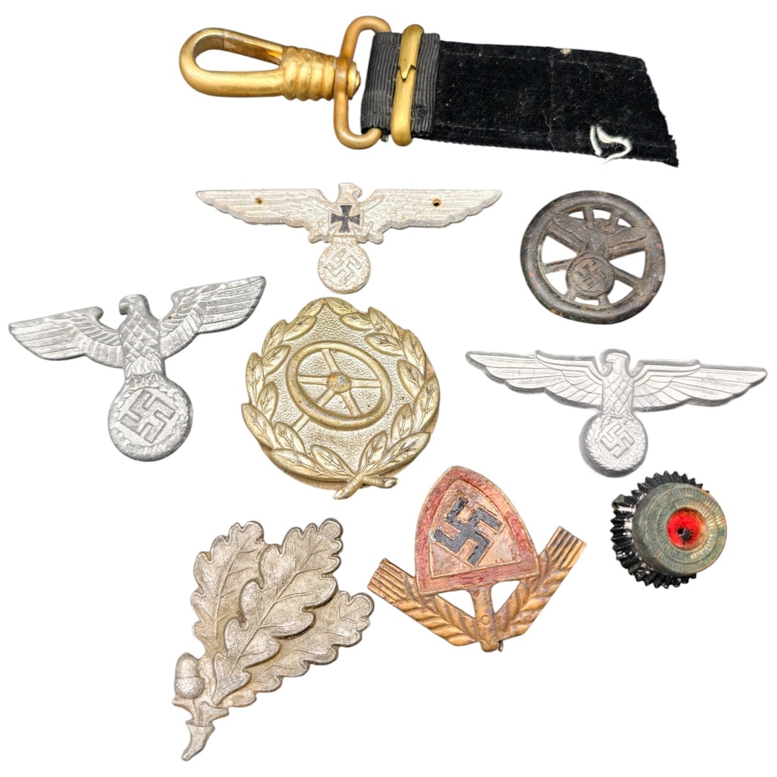 German WWII Wehrmacht Insignia: A mixed lot of German WWII era insignia including a set of aluminum cap eagles with swastikas, a metal breast eagle with swastika and Iron Cross detail, a gilt wreath and steering-wheel motorcorps-sty