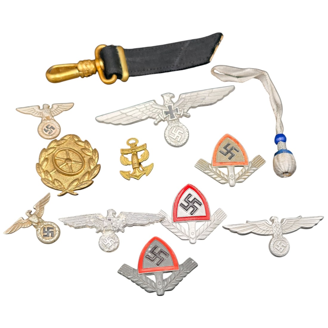 Grouping of German WWII Third Reich Insignia: A mixed lot of Third Reich-era metal insignia including cap eagles (Wehrmacht/Kriegsmarine style), Hitler Youth-type triangular cap badges with swastika motifs, a wreathed cockade-style badge, a small