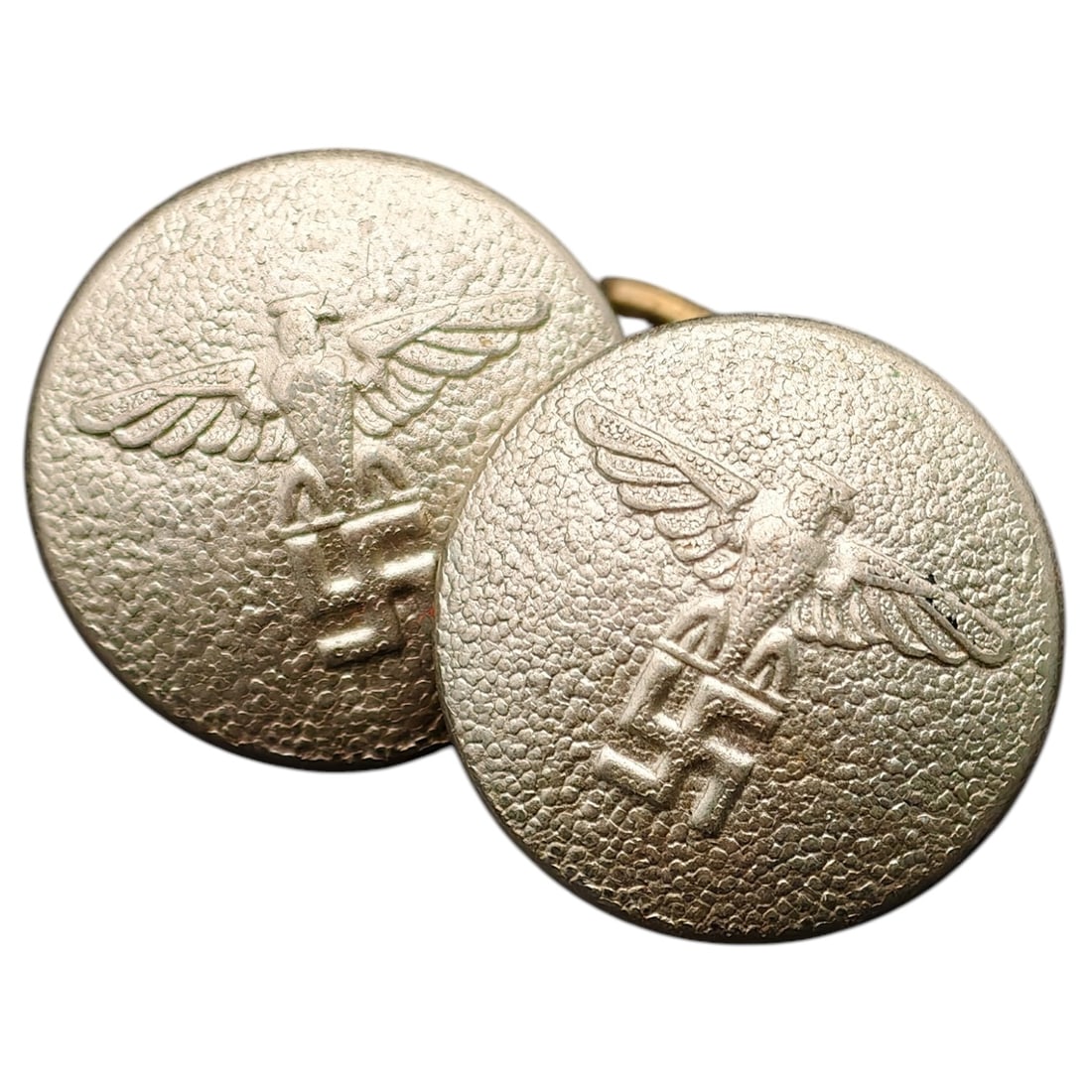 German WWII Linked Uniform Sleeve Button: A pair of domed metal uniform buttons joined by a brass wire link, each embossed with an eagle grasping a wreathed swastika, consistent with Third Reich-era service dress fittings. The buttons show a 