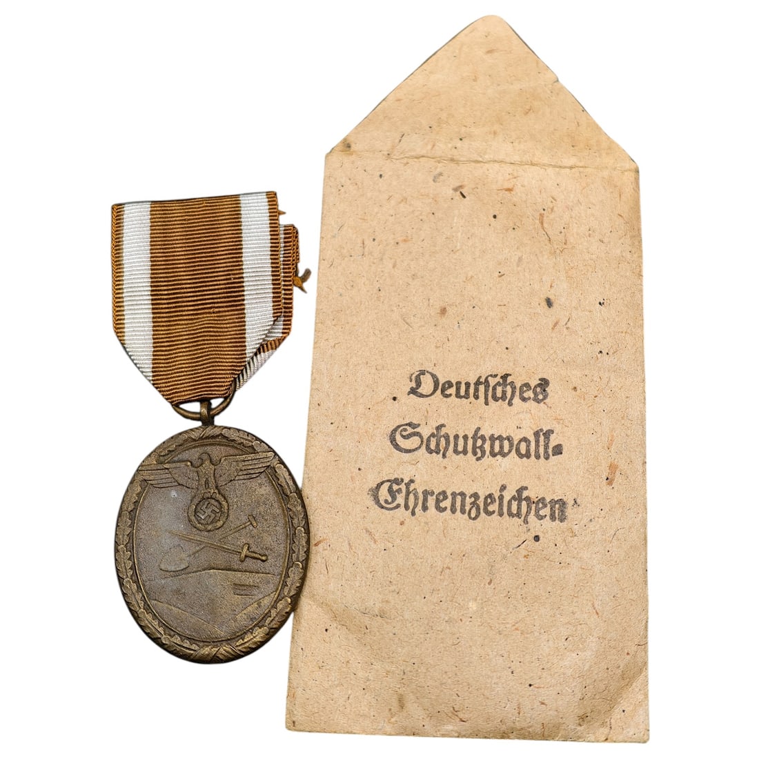Third Reich Westwall Medal Envelope: Medal in what appears to be bronze, oval in form, featuring an eagle clutching a mobile swastika above crossed sword and pick, with the reverse inscribed 'FÜR ARBEIT ZUM SCHUTZE DEUTSCHLANDS'. Suspen