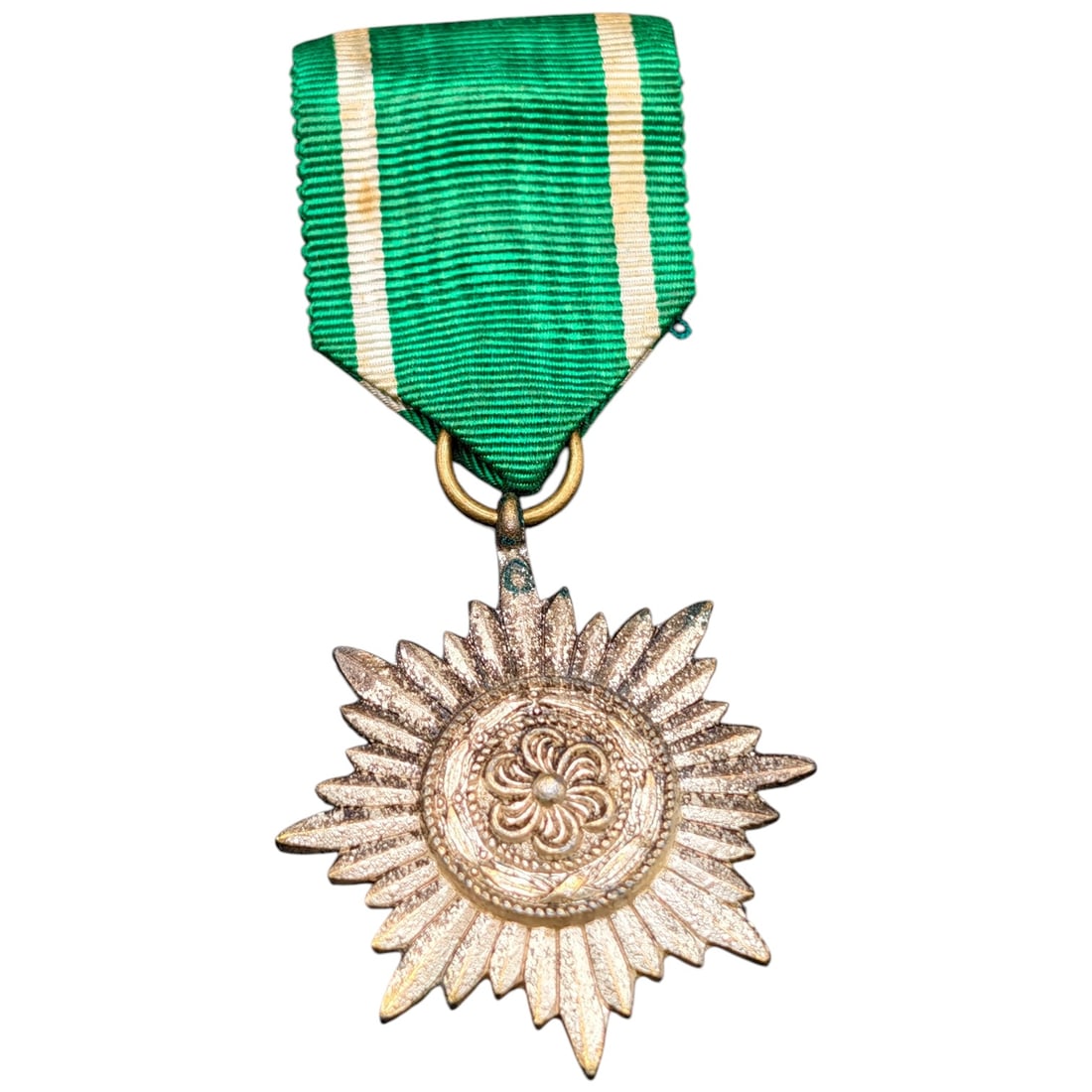 German WWII Ostvolk Medal of Merit, 2nd Class in Silver: A sunburst-form badge with a raised central rosette suspended from a triangular green ribbon with white edge stripes. The badge is struck as a multi-pointed radiating star, appears to be silvered meta