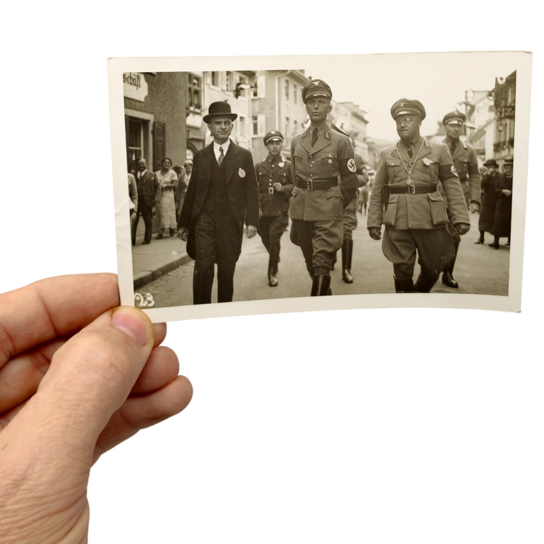 German 1935 Press Photo - Bürgerwehrfest with Ministerpräsident Köhler and SA Officials: A period gelatin silver press photograph depicting a street procession with a group of men in civilian dress and SA/party uniforms, several wearing swastika armbands, walking through a town lined with