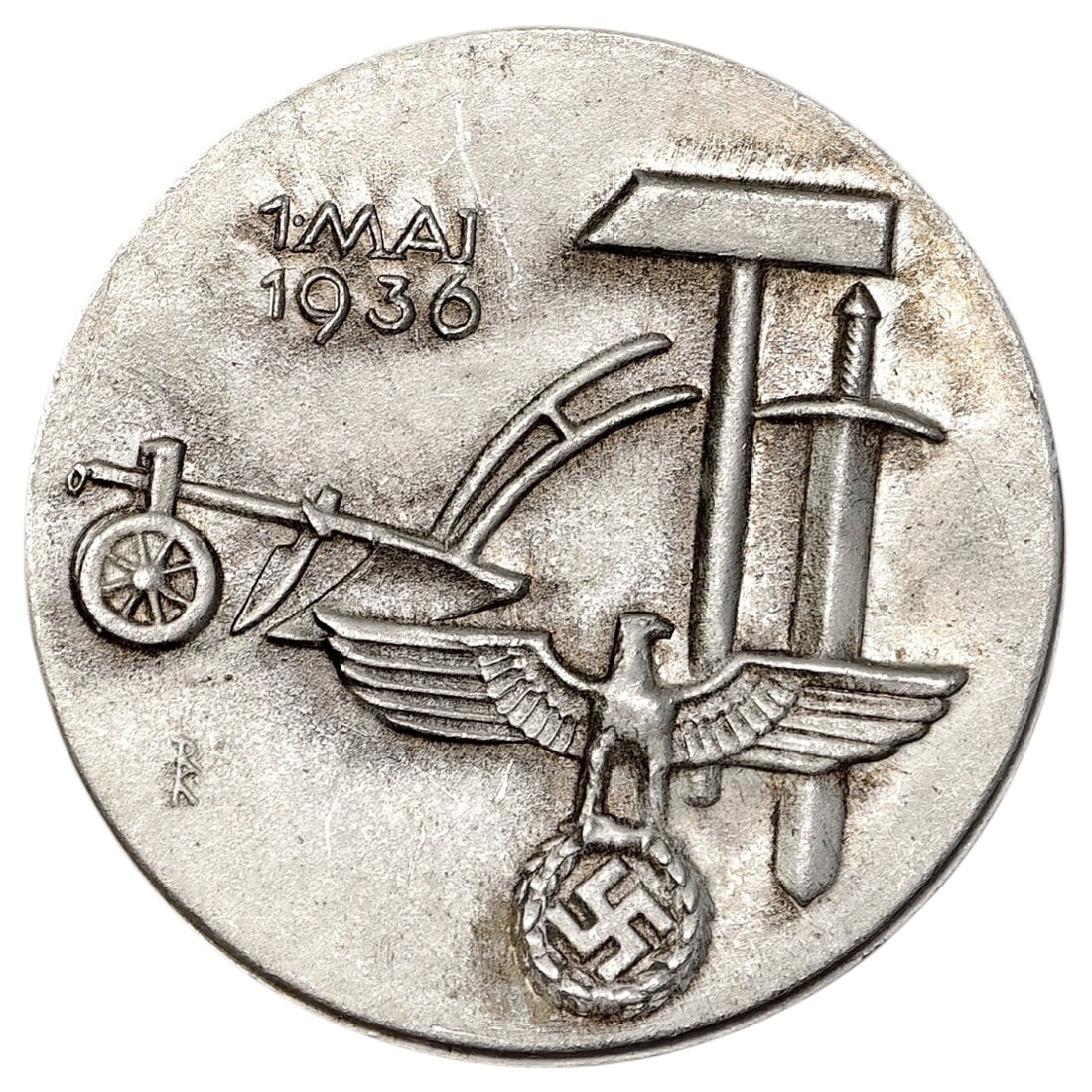 German 1936 National Labor Day (1. Mai) Tinnie Badge by Gebrueder Schmidt, Oberstein: A round tinnie badge marked "1. MAI 1936", combining a horse-drawn plough with a hammer, sword, and an eagle grasping a wreathed swastika. The design symbolizes the union of agricultural and industria