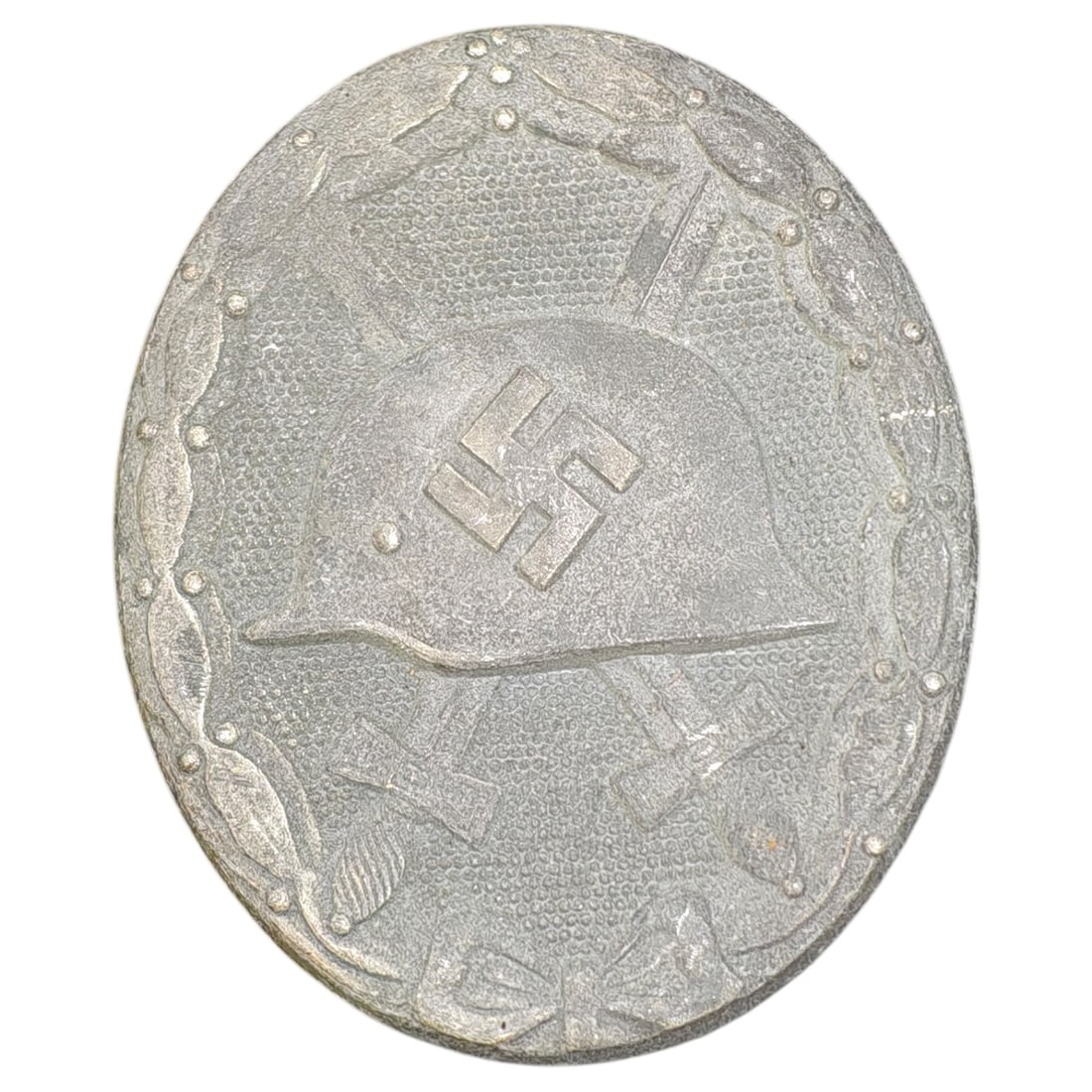 German WWII Wound Badge in Silver : An oval wound badge, depicting a stahlhelm over crossed swords set against a stippled field, surrounded by a laurel wreath tied at the base with a bow. This class of badge was awarded to German milita