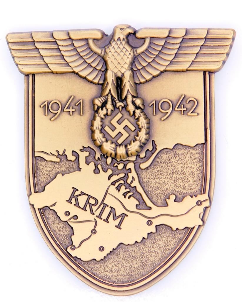 German WWII Army KRIM 1941 1942 Sleeve Shield: Excellent condition. Front shows a map of the Krim area. German eagle clutching a swastika in his talons at the top. It reads KRIM 1941 1942. Four flat vertical prongs on the reverse side. One piece d