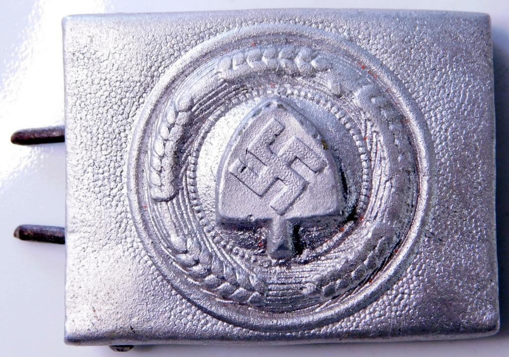 German WWII RAD Labor Korps EM Belt Buckle: One piece aluminum die struck construction. Front shows a shovel with a swastika in the center. They are surrounded by a round wheat stock border. Includes both prongs plus the belt hook on the back. 