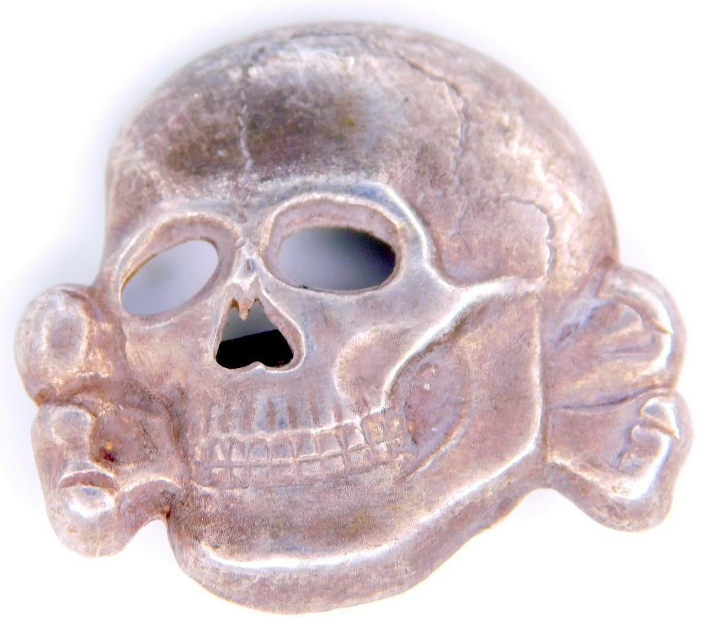 German WWII Waffen SS Officers Visor Cap Skull: One piece die struck stamped nickel construction. RARE. Front shows a Waffen SS skull and cross bones with the lower jaw. Reverse side is maker marked D. and S. M. ges. gesch., for the manufacturing f
