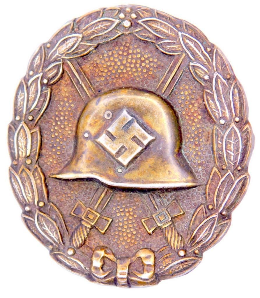 German WWII Silver Condor Legion Wound Badge: One piece die struck stamped nickel construction. Front shows the profile of a German helmet with a swastika in the center. Pair of crossed swords in the background. All three are surrounded by an ova