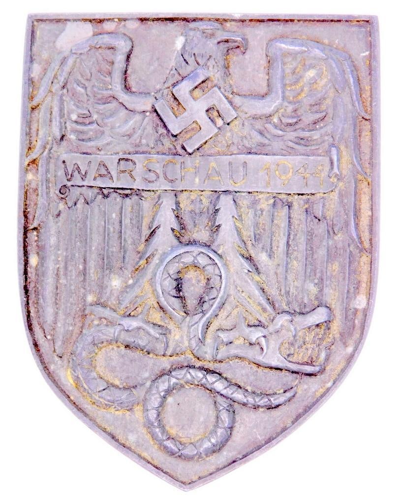 German WWII WARSCHAU 1944 Badge: One piece die struck metal construction. Front shows a spread winged German eagle with a swastika in the center of his chest. He is holding a snake in his talons. It reads WARSCHAU 1944. Thin vertical