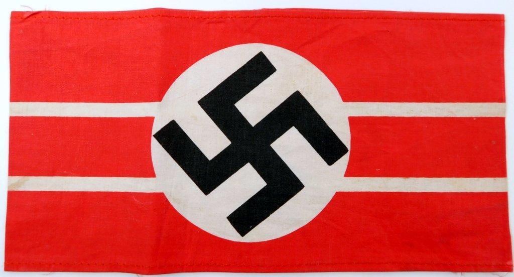 NSDAP Political Leader Swastika Arm Band: One-piece machine sewn printed cotton construction. Front shows a swastika in the center of a round white background. The outer rectangular arm band is a red base. Measures 8 3/8 inches wide by 4 5/16