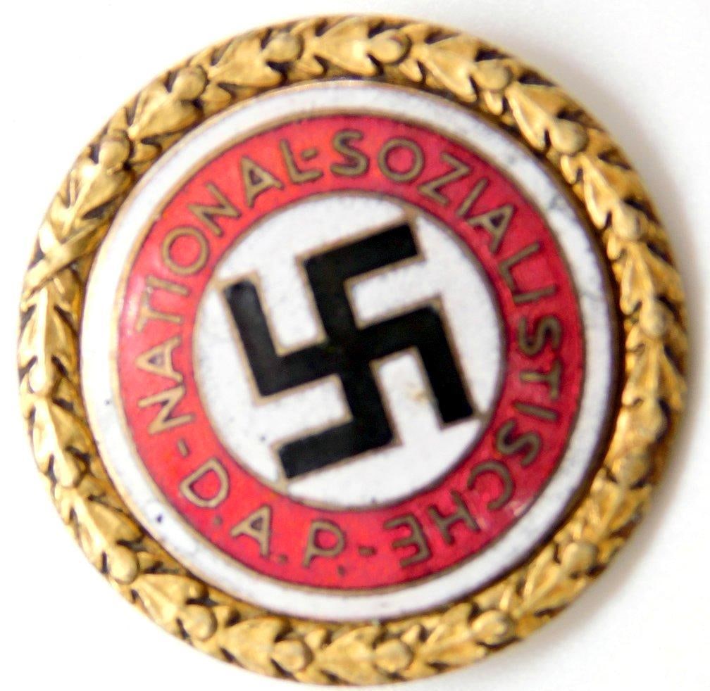 German WWII Political NSDAP Swastika Golden Party Badge: RARE. Front has a swastika in the center and reads National Sozialistische D. A. P.. The disc is surrounded by a round oak leaf wreath. Reverse is maker marked ges gesch Deutschler and Sohn Munchen 9.