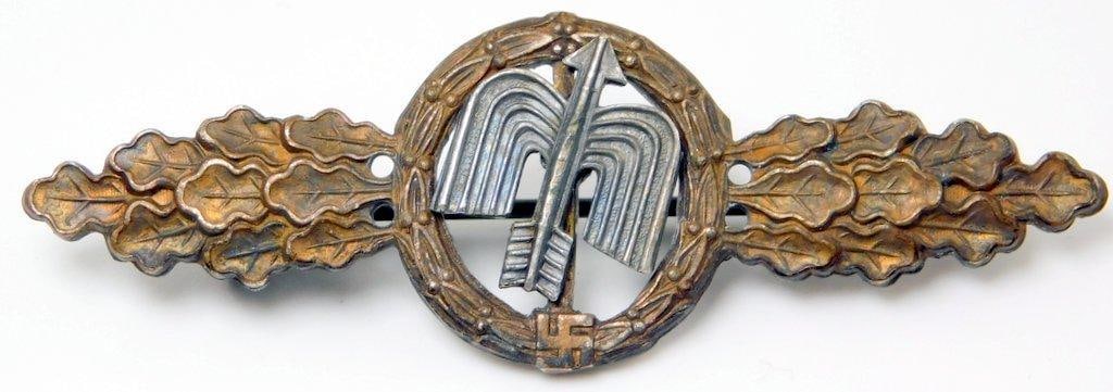 Luftwaffe Bronze Fighter Flight Clasp: Two-piece bronze and nickel construction. Front shows a winged arrow surrounded by a round oak leaf wreath. There is a swastika at the base. All three are flanked by oak leaves on each side. Thin hori