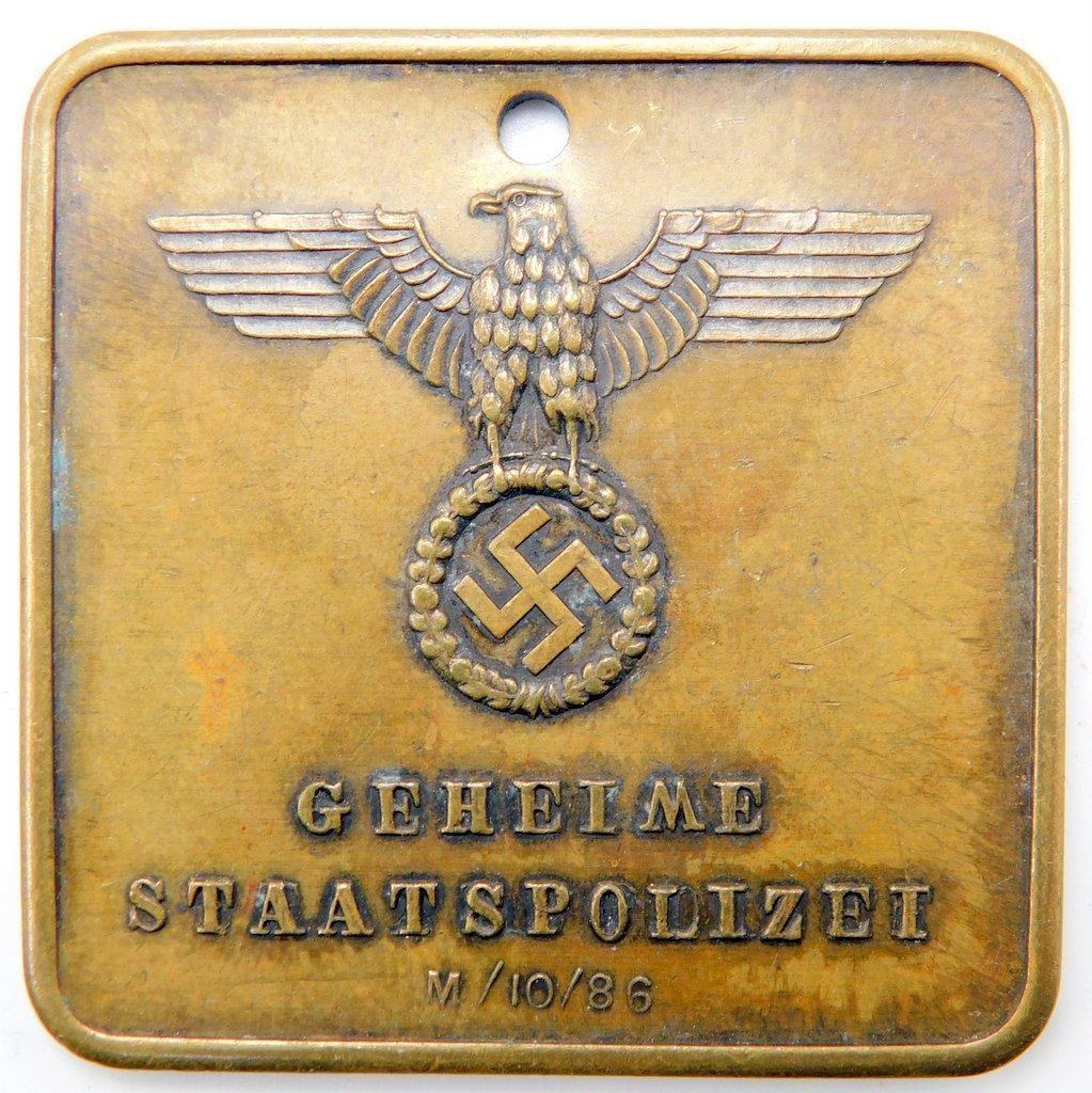 Waffen SS AUSCHWITZ Geheine Staatspolizei Criminal ID Disc: Die-struck brass construction. Front shows a German eagle clutching a swastika in his talons. Front side reads Geheime Staatspolizei M/10/86. Reverse reads Nr 9128 Auschwitz Zentral Inspektion. Measur
