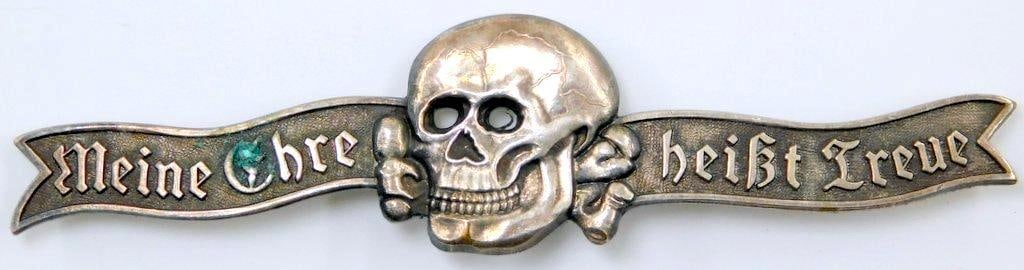 Waffen SS Skull and Cross Bones Lapel Bar: Front shows a Waffen SS skull and crossbones in the center. Reads Meine Ehre heist Treue (My Honor is Loyalty). Reverse is maker marked RZM M1/34. Thin horizontal pin back with a c-catch. One-piece di