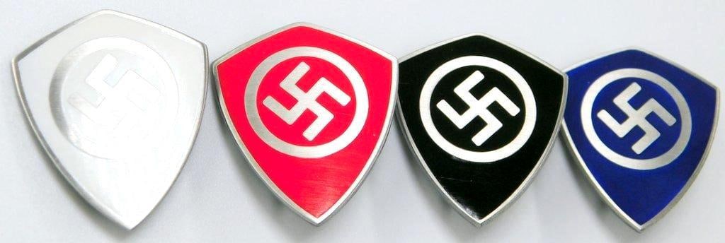German WWII Political Leader Swastika Lapel Badges, Four (4): One-piece die-struck nickel construction with enamel. Front shows a swastika in the center of a shield. Reverse is maker marked ges gesch. Thin vertical safety pin back. Measure 1 inches wide by 3/16 