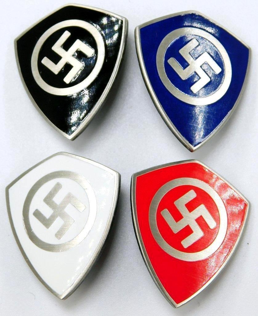 Swastika Shield Party Lapel Badges, Group of Four (4): One-piece die-struck nickel construction with enamel. Front shows a swastika in the center of a shield. Reverse is maker marked ges gesch. Thin vertical safety pin back. Measure 1 inches wide by 1 1/8