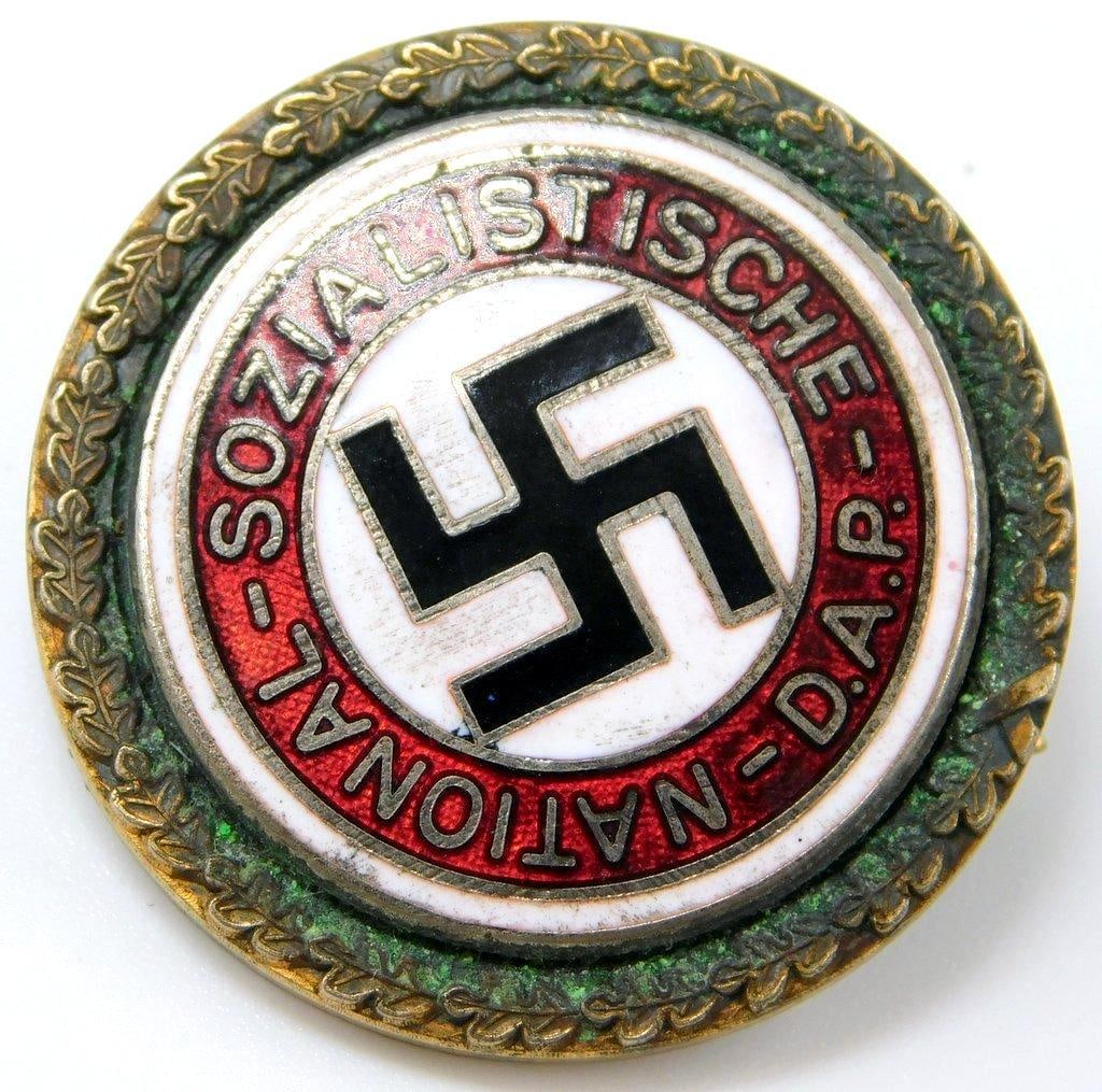 German WWII Political NSDAP Swastika Golden Party Badge: RARE. Two-piece die-struck brass construction with red, white, and black enamel. Front reads National Sozialistische D. A. P. There is a swastika in the center. Disc is surrounded by a round oak leaf 