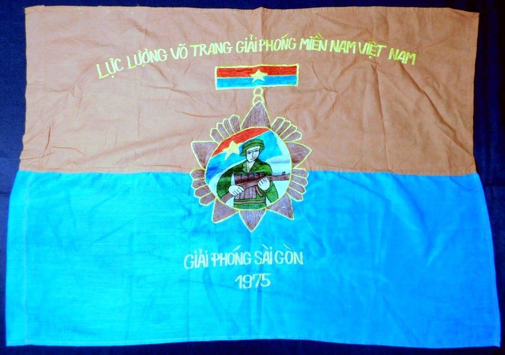VietNam Era Army Viet Cong 1975 VC Combat Battle Flag: Excellent condition. Two-piece machine-sewn and machine-embroidered construction onto a blue and orange cotton flag. Viet Cong soldier holding a rifle in the center. Reads LUC LUONGVO TRANG GIAPHONG M