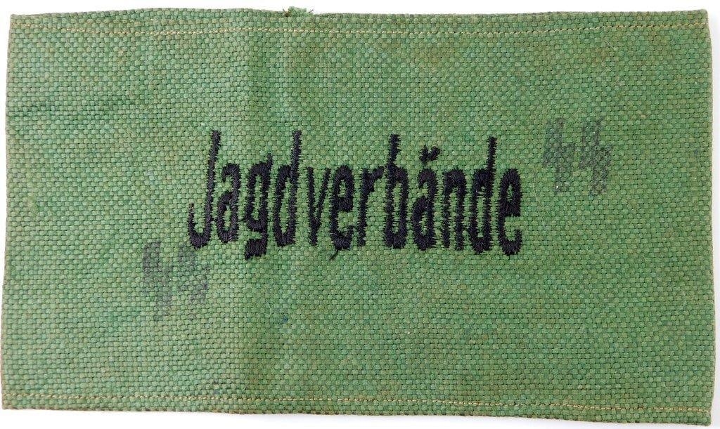German WWII Waffen SS Jagdverbande Arm Band: One-piece machine embroidered and machine-sewn cotton construction. Front reads Jagdverbande. Pair of Waffen SS runics stamped in black ink on each side. Measures 7 1/4 inches wide by 3 3/16 inches ta