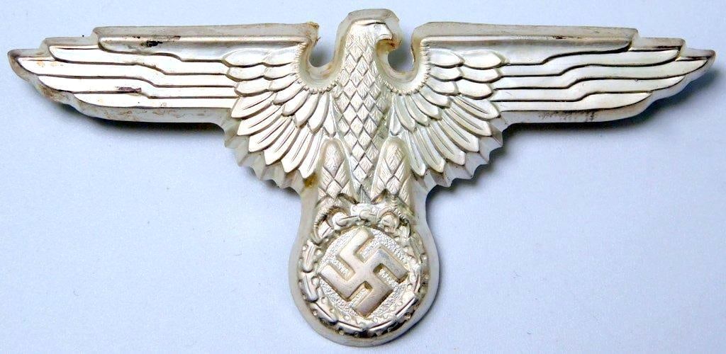Waffen SS Officers Visor Cap Eagle: One-piece die-struck stamped silver plated nickel construction. Front shows a Waffen SS eagle clutching a swastika in its talons. Reverse is maker-marked RZM M1/14. Two flat horizontal prongs on the b