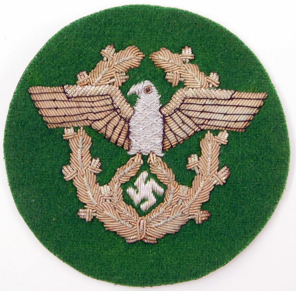 German World War II Police Officers Sleeve Eagle: Hand and machine-embroidered raised silver bullion wire onto a dark green wool base. This was to have been worn on the upper left sleeve of the officers uniform. Front shows a spread-winged German eag