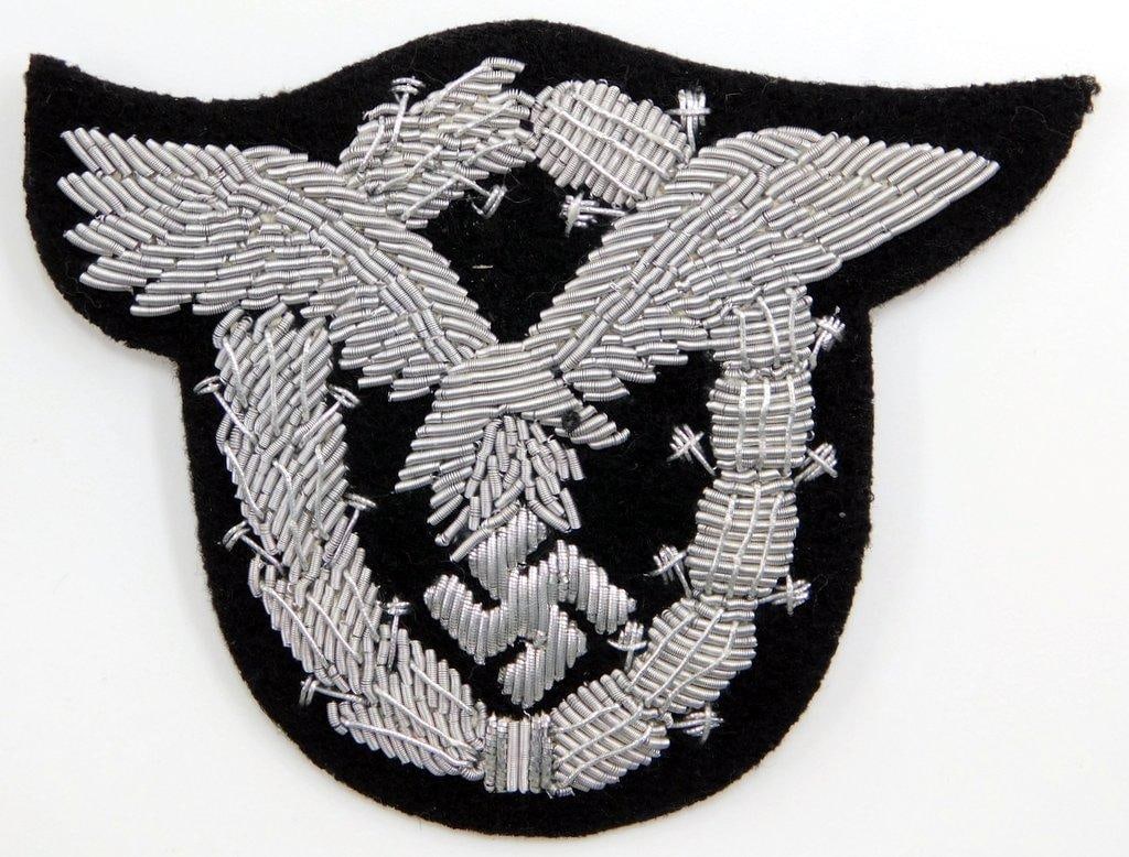 German WWII Luftwaffe Pilot Badge in Bullion Wire: Hand and machine-embroidered raised silver bullion wire onto a dark gray wool base. This was to have been worn on the left breast of the officers uniform. Front shows a spread-winged eagle clutching a