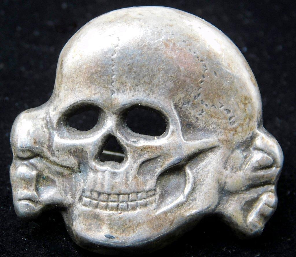 German WWII Waffen SS Officers Visor Cap Skull: One-piece die-struck stamped silver plated nickel construction. Front shows a Waffen SS skull and crossbones with the jaw. Reverse is maker-marked RZM SS 380/40. Two flat horizontal prongs on the back