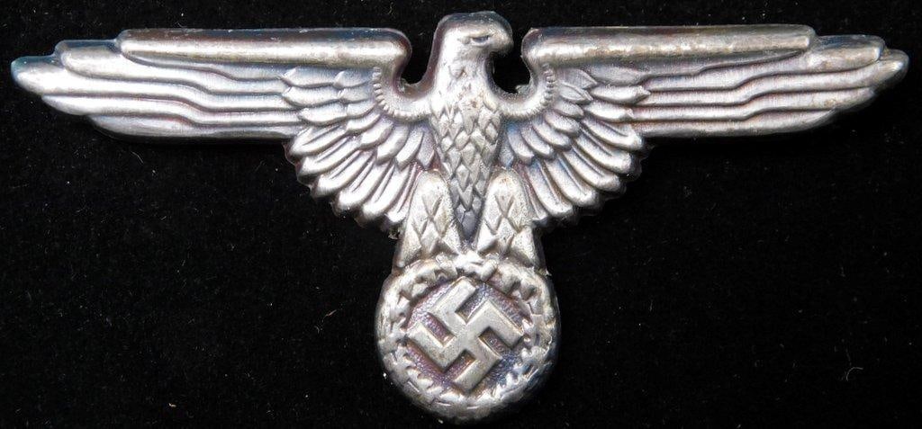 Waffen SS Officers Visor Cap Eagle: One-piece die-struck stamped silver-plated cupal construction. Front shows a Waffen SS eagle clutching a swastika. Reverse is maker-marked RZM. Two flat horizontal prongs with a copper finish on the b