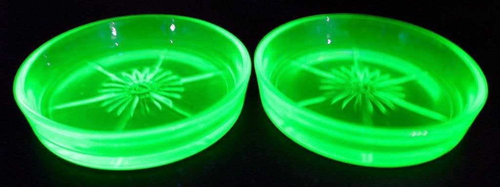 Set of Two (2) Coasters: Green uranium glass coasters featuring a geometric starburst design at the center The glass glows brightly under UV light due to its uranium content Each coaster has a slightly raised outer lip and