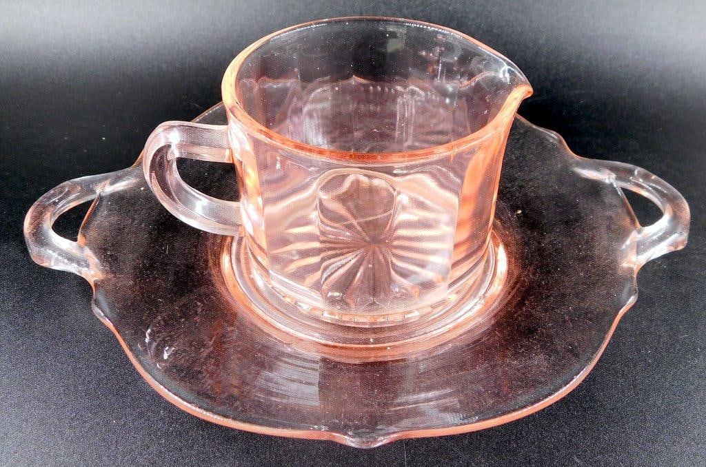 Depression Glass Pink Creamer and Handled Underplate: Depression-era pink glass set featuring a creamer and a handled underplate The creamer has a ribbed and starburst pattern, with a sturdy handle and spout The underplate also features a delicate
