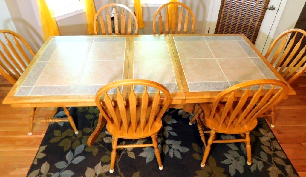 Oak Dining Table w/ Tiled Top and 6 Wooden Chairs: A solid oak dining table featuring a tile-inlaid top with decorative patterned borders The rectangular table is supported by a double pedestal base It includes six matching wooden chairs with