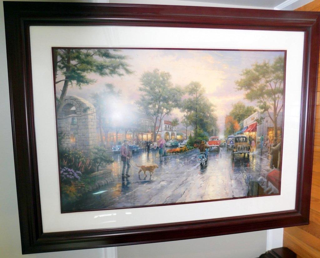 Thomas Kinkade 'Carmel, Sunset on Ocean Ave' Framed Artwork: Framed artwork by Thomas Kinkade titled Carmel, Sunset on Ocean Ave Features a street scene with pedestrians, vintage cars, storefronts, and lush landscapes under a sunset sky Includes artist
