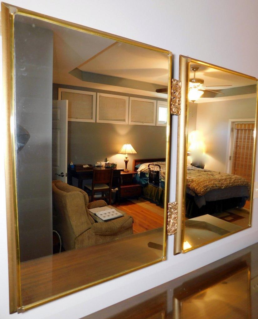 Wall-Mounted Gold-Tone Mirror w/ Two Section Joined by Ornate Center: Rectangular, gold-tone mirror featuring decorative floral-patterned center piece The mirrors are framed in a gold-colored material and are wall-mountable Some signs of wear or marks on the mirror
