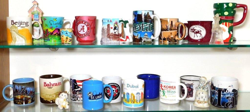 Souvenir Mugs From Various Locations Around the World: 18 souvenir mugs featuring locations such as Beijing, Seattle, Dubai, Korea, Bahrain, New Hampshire, St. Louis, Chicago, and more Designs include city skylines, landmarks, and cultural highlights All