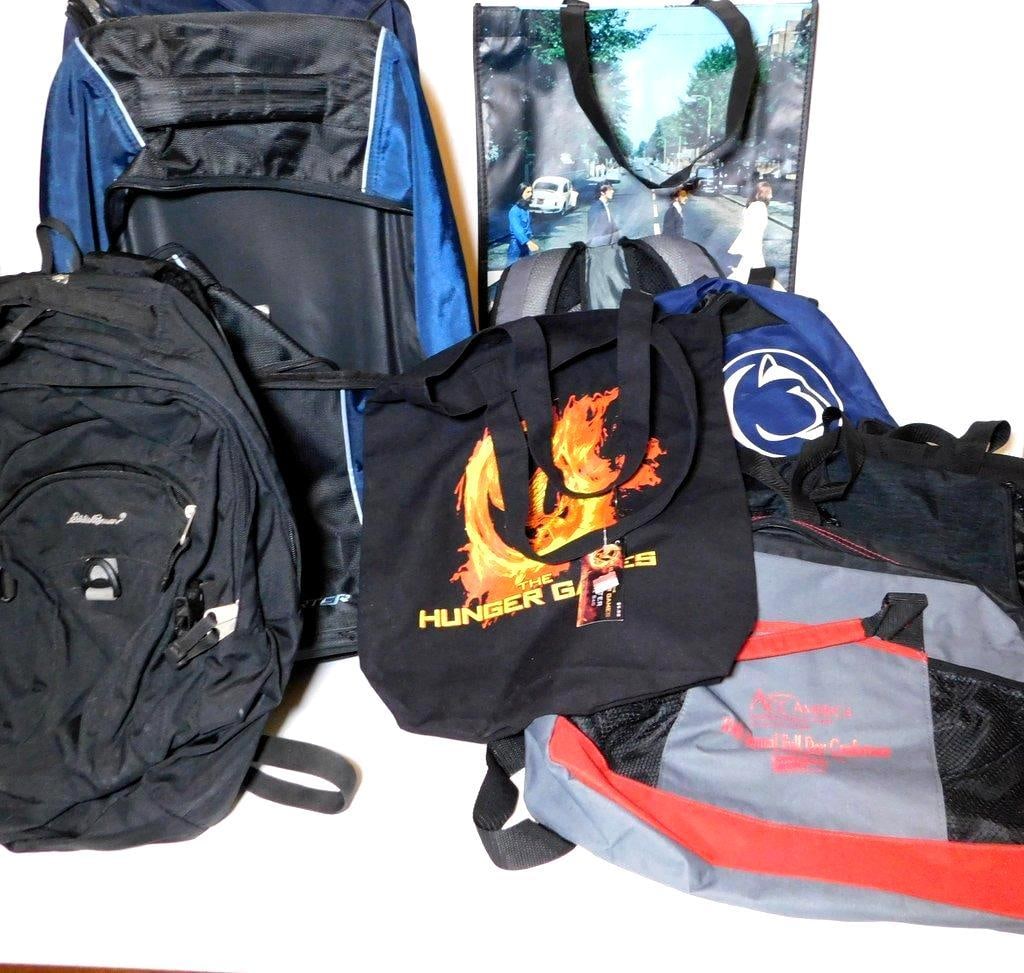 Backpacks and Bags Featuring Eddie Bauer, American Tourister, and More: Lot containing a variety of bags, including an Eddie Bauer backpack, an American Tourister rolling bag, a Nike backpack with Penn State branding, a Hunger Games canvas tote bag, a Beatles-themed tote 